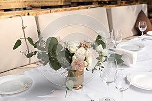 Wedding table setting decorated with fresh flowers in a brass vase. Wedding floristry. Banquet table for guests outdoors with a