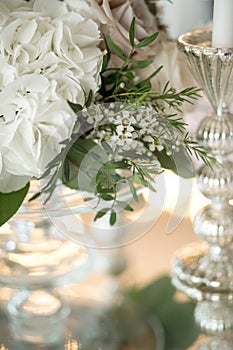 Wedding table setting is decorated with fresh flowers and white candles. Wedding floristry. Bouquet with roses, hydrangea and