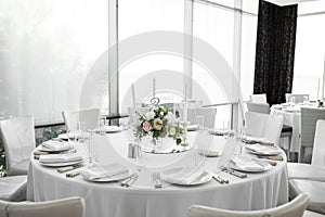 Wedding table setting decorated with fresh flowers. White plates, silverware, white tablecloth and white room. Wedding floristry.