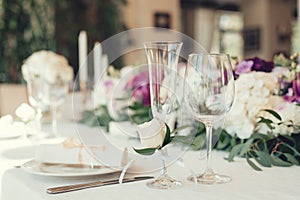 Wedding table settings with flowers decoration and candles, close up on whine glasses