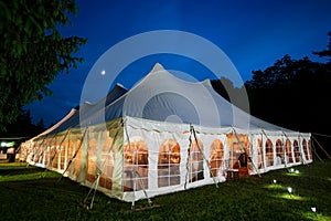 A wedding tent at night with blue sky and the moon. The walls are down and the tent is set up on a lawn - wedding tent series photo