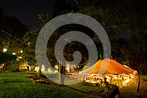 A wedding tent at night surrounded by trees with an orange glow from the lights. - wedding tent series