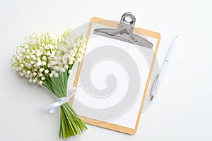 Wedding to do list concept. Clipboard with blank paper note, lily of the valley and pen on white background. Flat lay, top view