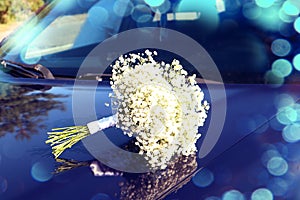 A wedding is a troublesome business: a delicate bouquet of the bride lies on the blue hood of a car, close-up, bokeh