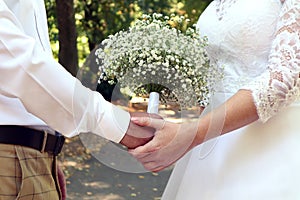 A wedding is a troublesome business: a delicate bouquet in the hands of the bride and groom against the background of the park