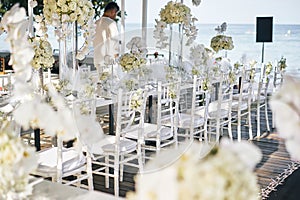 The wedding venue for reception dinner table decorated with white orchids, white roses, flowers, floral, white chiavari chairs