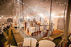 Wedding venue tent with dinner equipment on tables and string lights