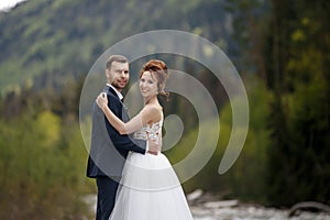 Wedding walk. The bride and groom walk along the river bank, holding each other`s hands. Portrait of the bride and groom