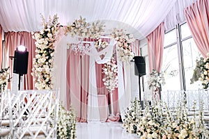 The wedding zone is decorated with white and peach cloth, crystal chandelier, transparent chairs for guests and beautiful floral a