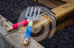 Weed fork and double sided hoe and rake garden hand tools on wooden vegetable planter box edge.
