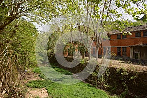 Weedy riverway before deserted 1970s` red brick workshop in sunny spring photo