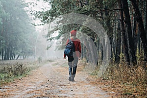 Weekend breaks and getaways in forests. Stay close to nature. Young woman in red hat and sweater with backpack