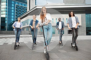 Five friends having ride on motorized kick scooters