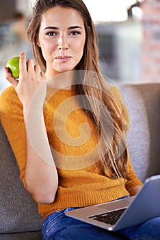 Weekend munchies on the sofa. an attractive young woman relaxing on the sofa with her laptop.