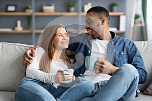 Weekend Pastime. Happy Mixed Couple Relaxing On Couch With Coffee At Home