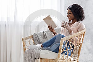 Weekend Pastime. Young Black Woman Relaxing In Armchair With Book And Coffee