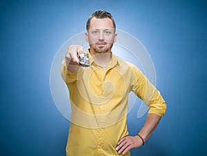 Weekend time. Man holding remote control and watching TV - movies over blue background, dresses in yellow shirt. Front view of guy