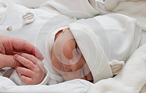 weekly baby holds hand. Baby wearing a white clotheslying. Infant just borned, have a one week photo