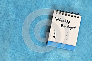 Weekly budgeting concept. White note pad isolated on blue background.