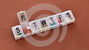 A weekly medicine dispenser opened for Monday, prescription pills and vitamins in a white pill box on terracotta