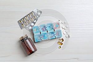 Weekly pill box and bottle with medicaments on white wooden table, flat lay