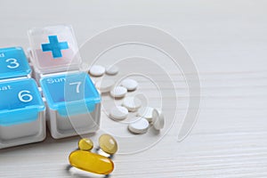 Weekly pill box with medicaments on white wooden table, closeup. Space for text