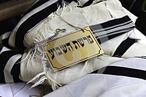 Weekly Torah reading sign in Hebrew lying on a prayer shawl