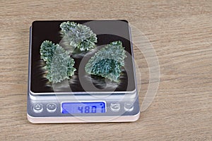 Weighing of rare moldavite gems by scale with digital display on a wood background
