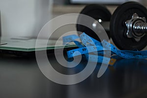 Weighing scale and  measuring tape with dumbbell on the side on black table background.