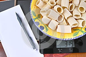 Weight control - black glass kitchen scale with Italian pasta, pencil and paper