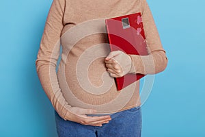 Weight gain during pregnancy, pregnant woman holding scale, faceless future mommy against blue background touching her belly,