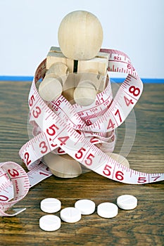 Weight loss concept with wooden man wrapped in a measuring tape and diet pills