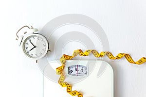 Weight loss control planning. White scale and measuring tape and timing alarm clock