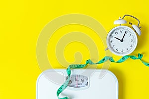 Weight loss control planning. White scale and measuring tape and timing alarm clock for body dieting healthy life.