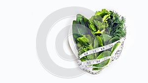 Weight loss diet. Fresh green leaf lettuce, spinach, sorrel, dill and measuring tape on heart shaped plate on white background.