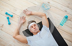 Weight loss from effective workout. Tired athlete with dumbbells and rope lying on mat and takes breath