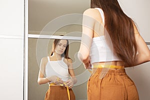 Weight loss, A girl in front of a mirror with a measuring tape looks at the figure, whether the size has decreased