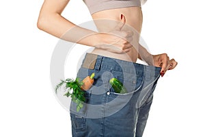 Weight loss and healthy eating or dieting concept. Slim girl in oversized jeans with raw vegetables in the pockets