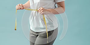 Weight loss, slim body, healthy lifestyle concept. Fit fitness girl measuring her waistline with measure tape on blue