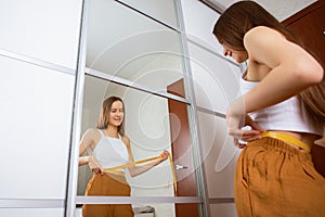 Weight loss. A teenage girl at home in front of a mirror examines her waist after dieting and playing sports, rejoices in a thin