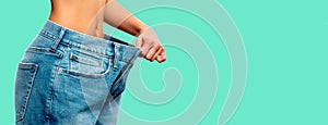 Weight loss. Woman in oversize jeans on green background