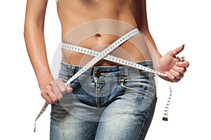 Weight loss - woman with trained belly. Young skinny female in blue jeans with slim body is measuring her waist with tape measure