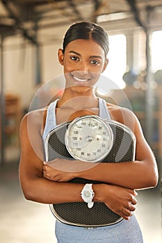 Weight to go on your diet goals. Portrait of a fit young woman holding a scale in a gym.