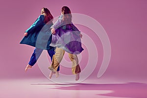 Weightlessness, ease of movement. Young stylish fashionable woman dancing contemp isolated over crystal pink background