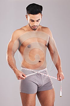 Weightloss, fitness and man with measure tape standing in a studio with a gray background. Health, strong and athlete