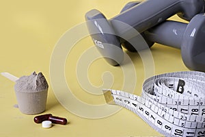 Weights and a tape measure along with pills and dietary supplements on yellow background. Sport supplements. Healthy diet concept