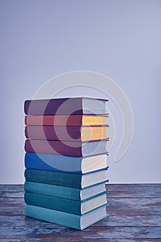 A weighty stack of bright smart books in textural fabric multi-colored covers on an old wooden table on a light background.