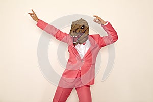 Crazy young guy wearing pink suit and funny dinosaur mask dancing and having fun at party