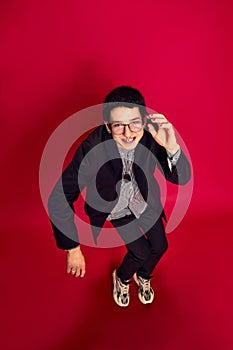 Portrait of stylish young man with glasses in strange pose over red background. Concept of student life, enjoying life