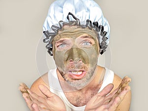 Weird looking man with shower cap and cream on his face horrified seeing himself ugly on bathroom mirror applying facial mask male